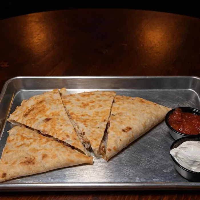 A quesadilla cut into wedges with salsa and sour cream