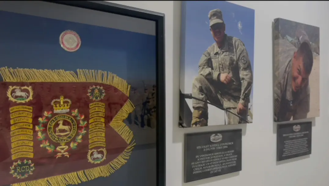 Part of the memorial wall at Over The Horizon: regimental colours and framed tributes to fallen service members